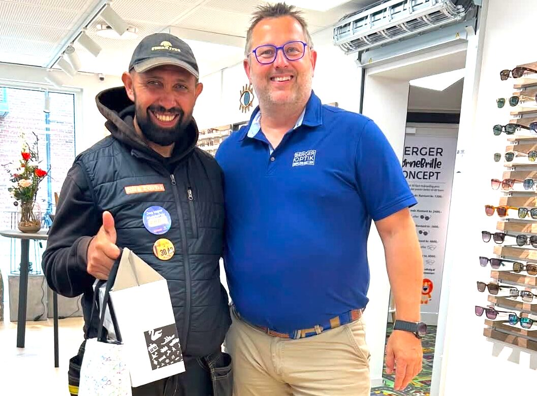 Ion står med en gavepose ved siden af optiker Christian Berger i Berger Optiks butik i Galten