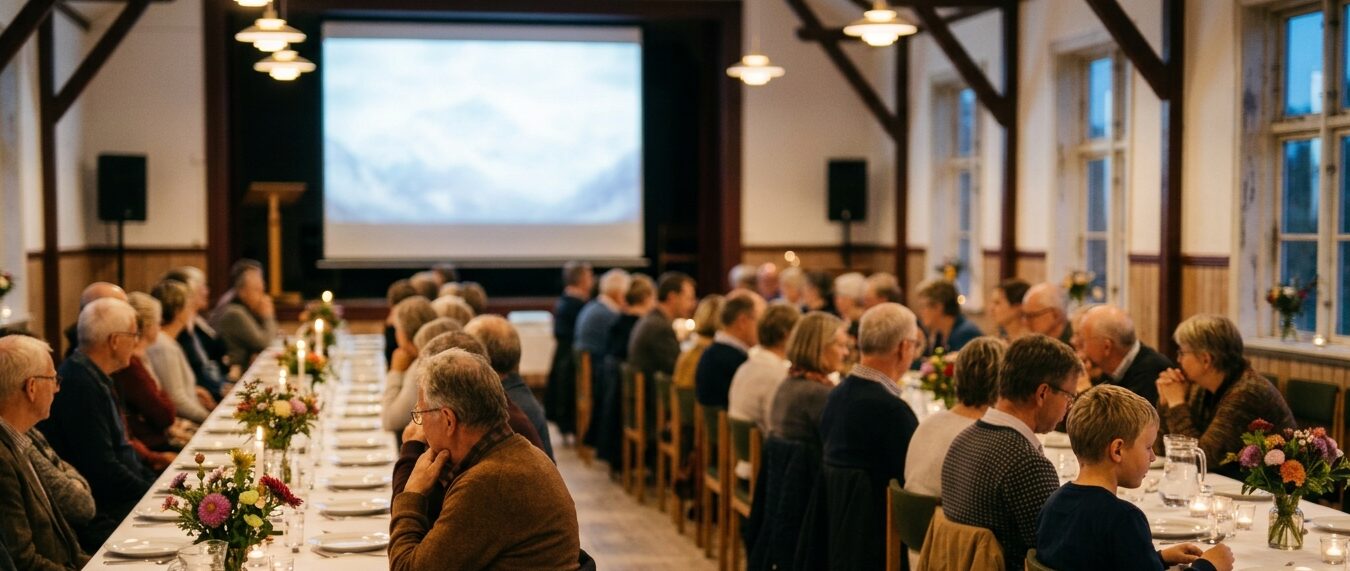 Gæster ved lange borde i forsamlingshus ser mod lærred med billede af Himalayas bjerge